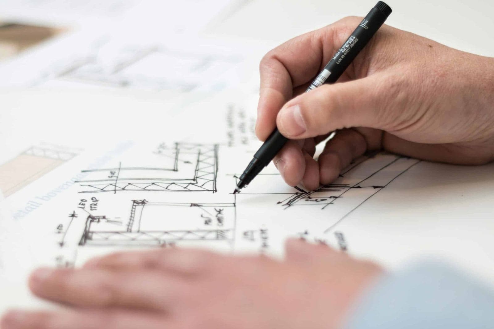 A hand using a black pen to draw a technical sketch on paper